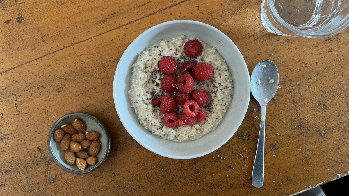 A bowl of overnight oats topped with raspberries and chia seeds next to a small dish of almonds on a wooden table