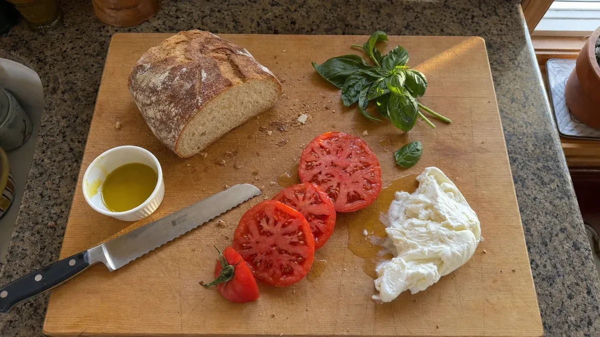 Fresh no-cook summer dinner with sliced tomatoes, mozzarella, and crusty bread on a wooden cutting board